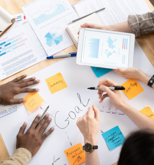 Above view of multi-ethnic colleagues standing around desk and working on business plan together at meeting